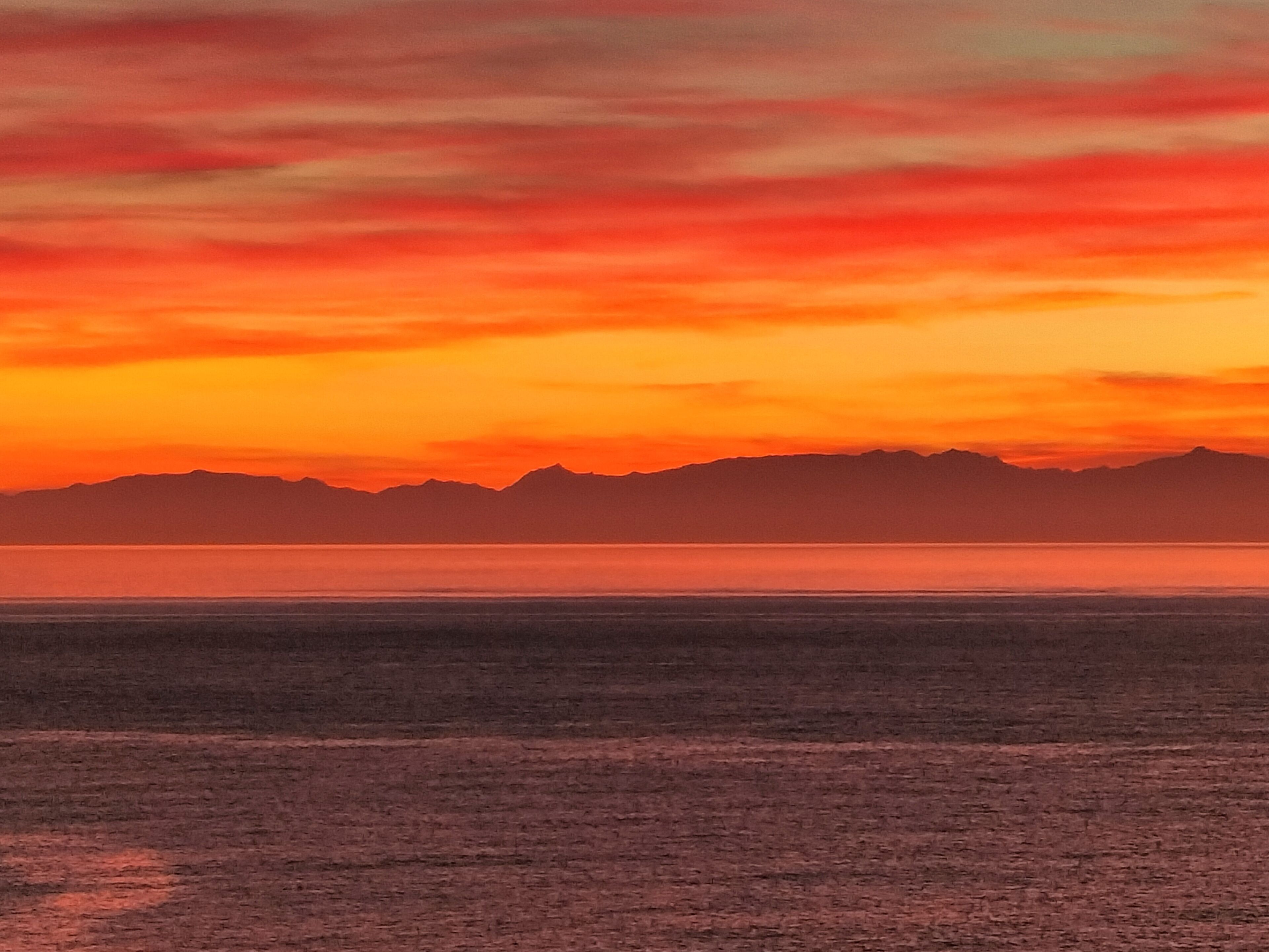 A sunset over a flat landscape with distant mountains.