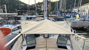 A boat deck with a covered seating area, a steering wheel, and a view of the marina with other boats and buildings in the background. - DREAM CRUISES SANTORINI,CYCLADES,MYKONOS, ON LUXURY SAILBOAT WITH HOSTESS/CHEF (Athina)