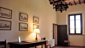 A room with a wooden table, a chair, a lamp, and framed pictures on the wall. - XIII century Castle overlooking an uncontaminated valley. (Gualdo Cattaneo)