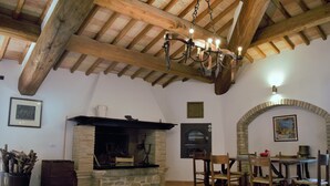 A rustic dining area with a stone fireplace, wooden beams, and a hanging light fixture. - XIII century Castle overlooking an uncontaminated valley. (Gualdo Cattaneo)