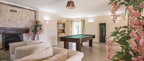 A living room with a pool table, beige sofa, and a fireplace.