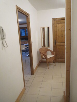 Un pasillo con una puerta de madera, una silla de mimbre y un teléfono en la pared.