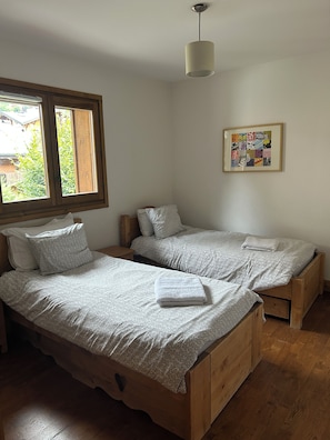 A bedroom with two wooden beds, a window, a ceiling light, and a wall-mounted picture.