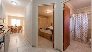 Une chambre d’hôtel comprenant un lit, une salle de bain avec un rideau de douche, un coin repas avec une table et des chaises, et un coin cuisine avec une cuisinière.