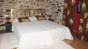Un lit avec une tête de lit en bois, deux tables de chevet avec des lampes et un mur en pierre.