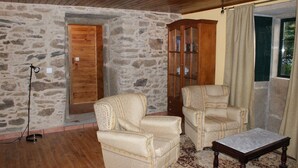 Une pièce aux murs de pierre, avec deux fauteuils, un buffet en bois, une petite table et un plancher en bois.