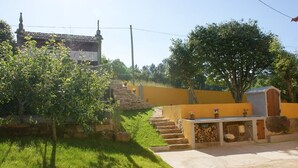 Une cour avec un escalier en pierre menant à un bâtiment jaune, entouré de verdure et d’un petit abri de jardin.
