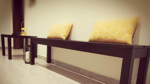 A bench with two yellow patterned cushions against a wall.