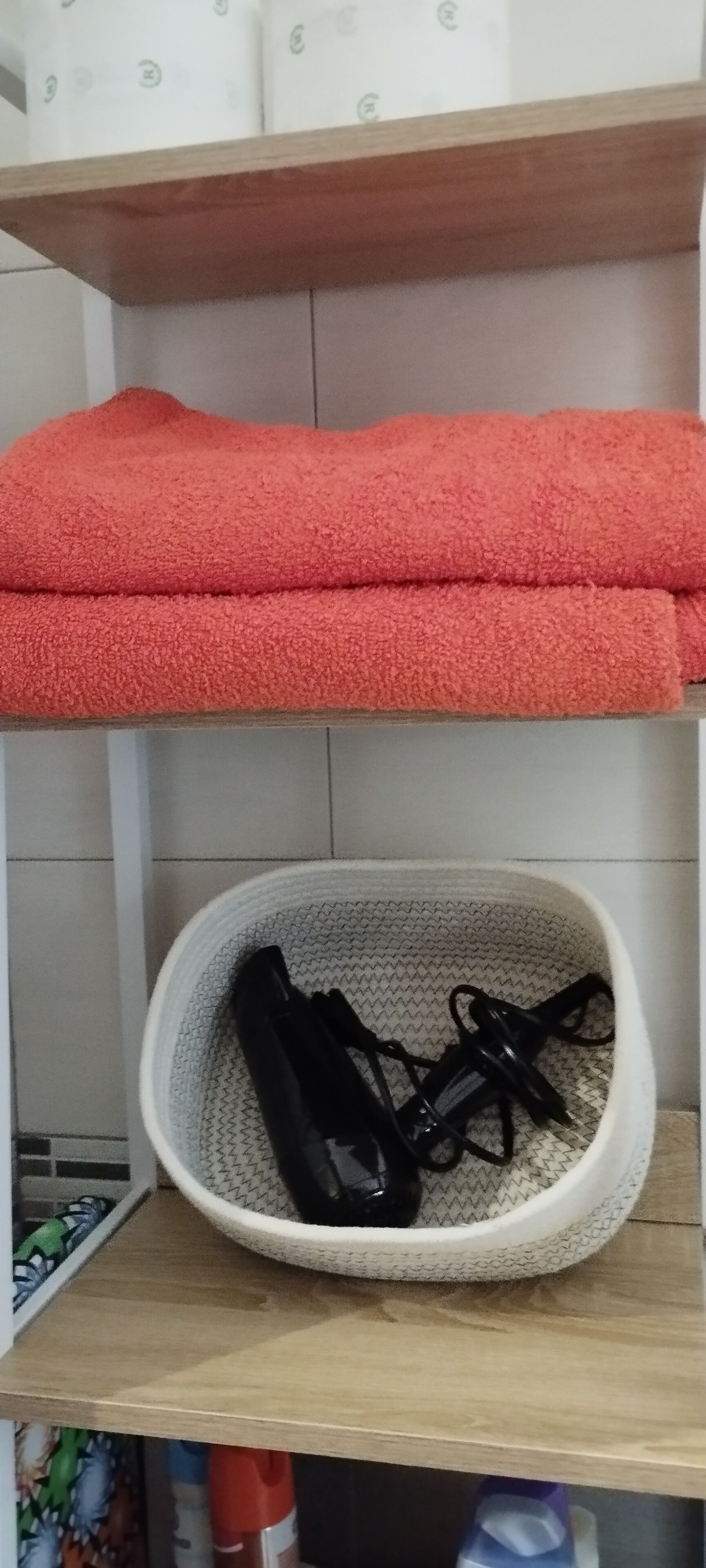 A shelf with a red towel and a white basket containing black shoes.