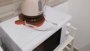 A coffee maker on a white microwave, with a tiled wall in the background.