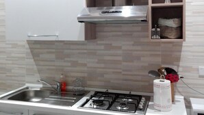 A modern kitchen with a stainless steel sink, a gas stove, and a microwave. There are cabinets with handles and a small shelf with decorative items.