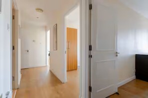 Un couloir doté d’un plancher en bois, de murs blancs et d’une porte fermée sur le côté droit.