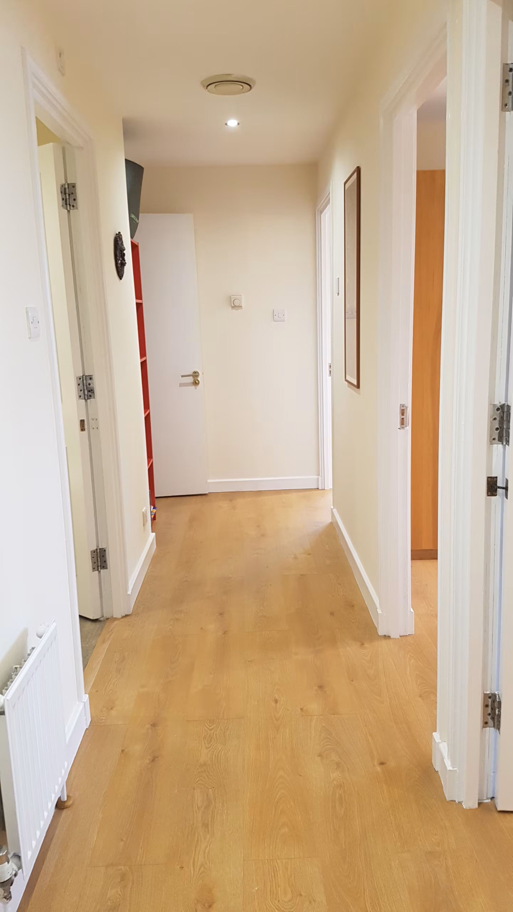 Un couloir doté d’un plancher en bois, de murs blancs et de portes donnant sur d’autres pièces.