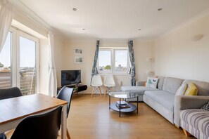 A living room with a sofa, a dining table, chairs, a TV, and a window with curtains. - Beautiful 2-bedroom apartment, close to Portobello Market (London)