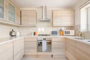 A modern kitchen with light wood cabinetry, stainless steel appliances, and a central island.