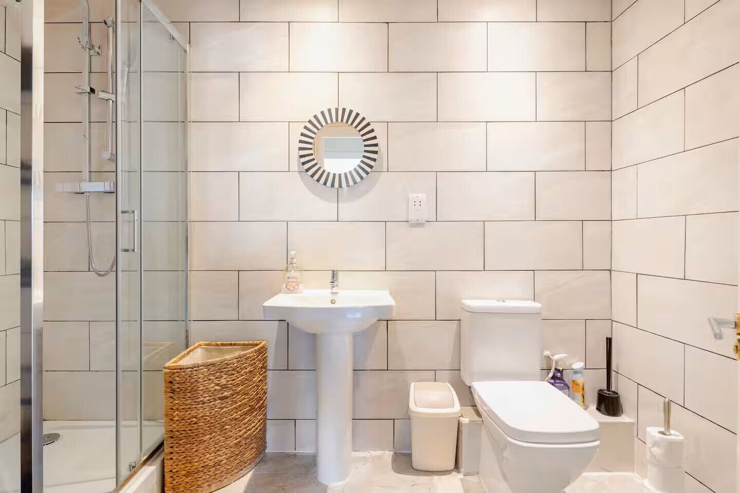 Een moderne badkamer met een douchecabine van glas, een wastafel op een voetstuk, een toilet en een decoratieve spiegel.