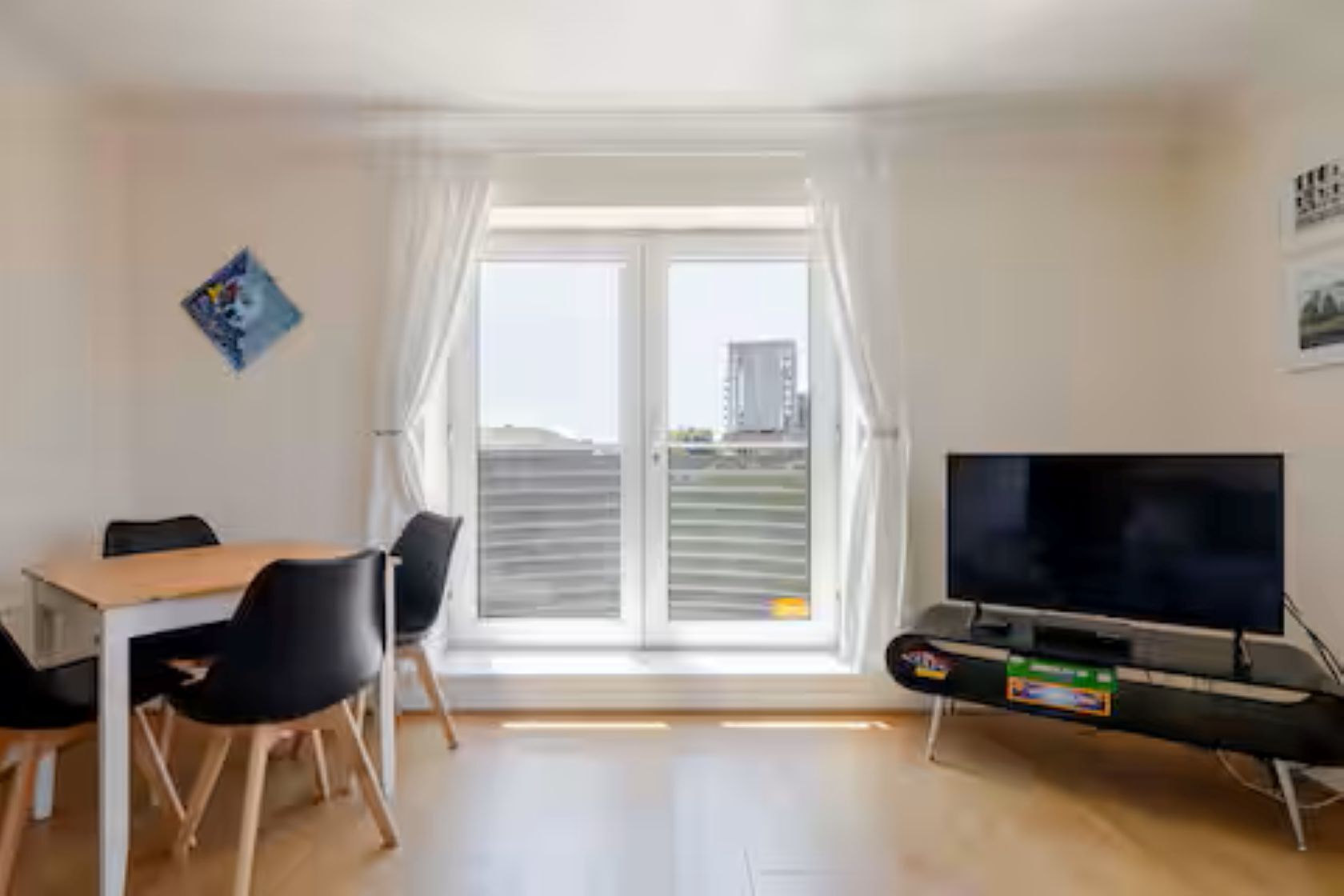 A room with a dining table, chairs, a flat-screen TV, and a sliding glass door leading to a balcony.