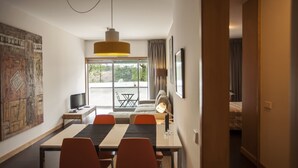 Una moderna camera d'hotel con zona pranzo, un'ampia finestra con tende, televisore a schermo piatto e un letto con vista.