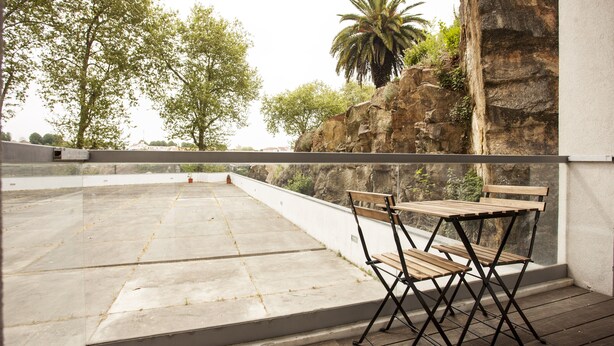 Una terrazza sul tetto con un tavolo e sedie di legno, un muro in pietra e una palma.