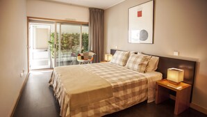 Una camera d'albergo con un letto grande, un comodino con una lampada, una sedia e una porta finestra che dà su un balcone.