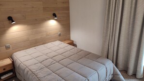 A bedroom with a wooden headboard, a bed with a beige quilt, and two wall-mounted lights.