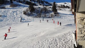 A ski slope with skiers and a stone building in the foreground.