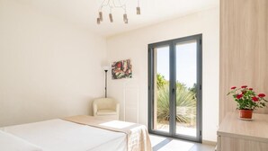 A modern bedroom with a bed, a chair, a floor lamp, a painting, and a view through a sliding door. - Villa Lavanda and Il Mandorlo - Near Noto (Noto)