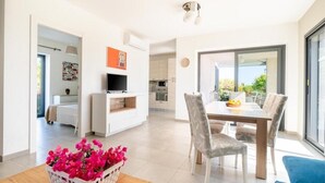 A modern living room with a dining area, a TV, and a kitchen in the background. - Villa Lavanda and Il Mandorlo - Near Noto (Noto)