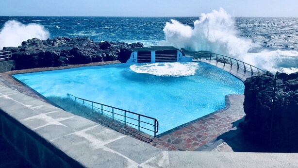 Ein Pool mit Blick auf den Ozean, umgeben von felsigem Gelände und einem Geländer.