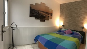 Ein Schlafzimmer mit einem Bett, einem Wandbild, einer Stehlampe und einem Fenster.