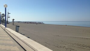 A beach with a paved walkway, umbrellas, and a pier in the distance. - Luxury 3 bed apartment, on sea front, sleeps 6 (Torrox-Costa (Malaga))