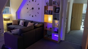 Un salon moderne avec une grande horloge murale, un canapé, une bibliothèque et une porte donnant sur une autre pièce.