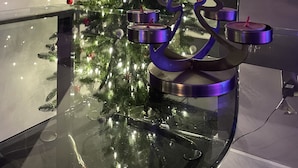 Un sapin de Noël décoré de guirlandes lumineuses et d’ornements, une étoile en guise d’ornement et un chandelier posé sur une table en verre.