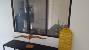 Ein modernes Interieur mit einem großen Spiegel, der eine Küche widerspiegelt, einer Holzskulptur auf einem schwarzen Tisch und einem gelben Schild mit Text.