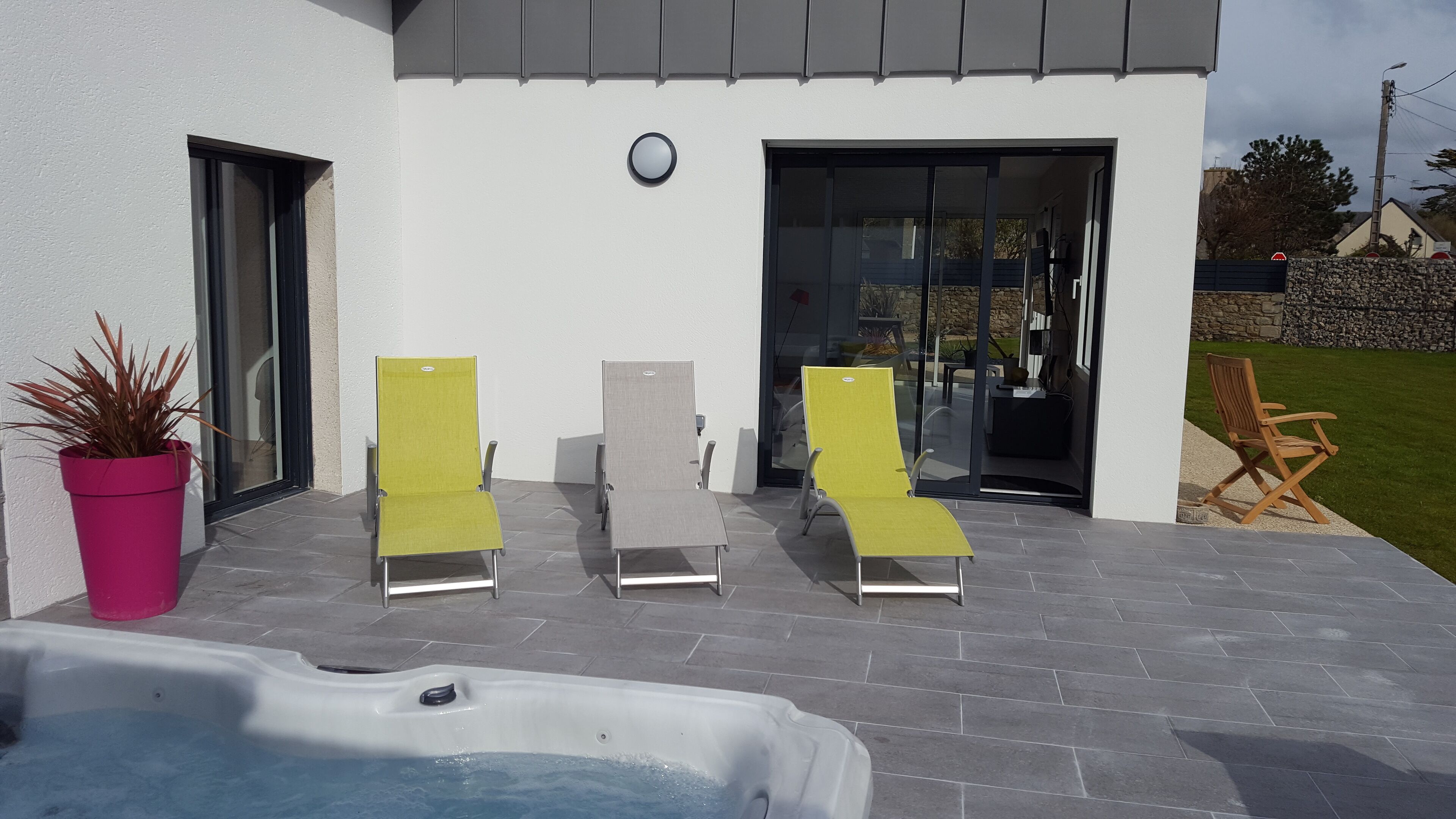 A modern outdoor area with a hot tub, two lounge chairs, and a potted plant.