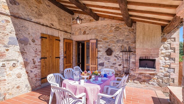 Un patio al aire libre con paredes de piedra, una mesa lista para comer, una puerta de madera y una chimenea.