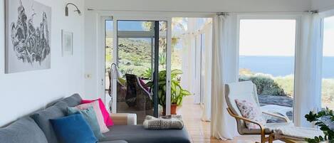 Un salón amplio con un sofá grande de color gris, una mesa de centro y vistas al océano a través de amplias ventanas.