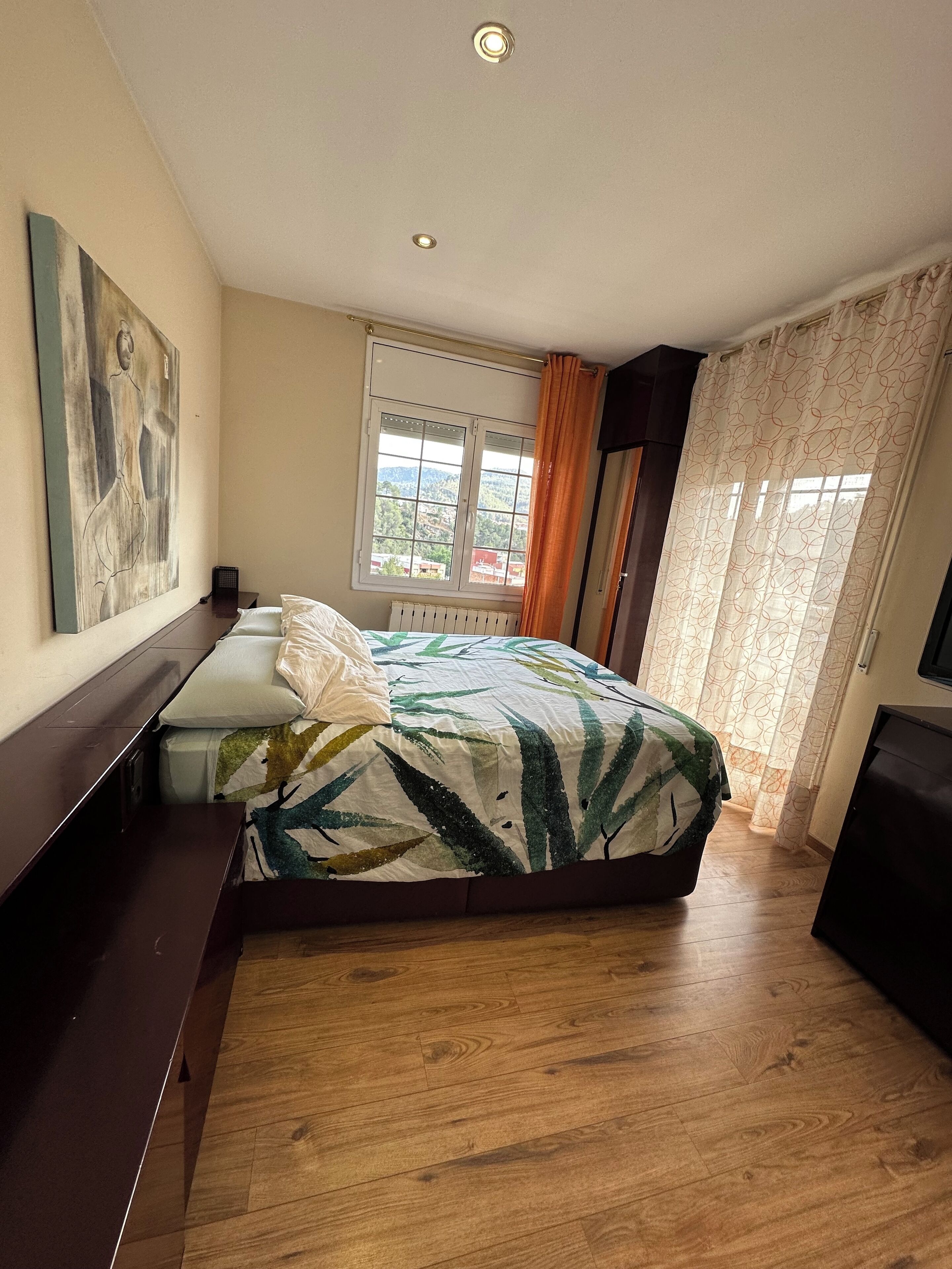 A bedroom with a bed, a nightstand, a dresser, a window with curtains, and a painting on the wall.