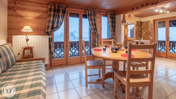 Ein gemütliches Zimmer mit Holzboden, einem runden Esstisch mit Stühlen, einer Couch und einem Heizkörper.