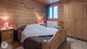Ein Schlafzimmer mit Holzwänden, einem Bett, Nachttischen, einem Schminktisch und einem Fenster mit Vorhängen.