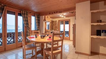 Un comedor acogedor con una mesa y sillas de madera, una cocina al fondo y un balcón con barandilla.