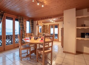 A cozy dining area with a wooden table and chairs, a kitchen in the background, and a balcony with a railing.