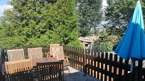 Un espace extérieur aménagé avec des meubles en bois, comprenant une table et des chaises, entouré d’une clôture en bois et agrémenté d’un parasol.