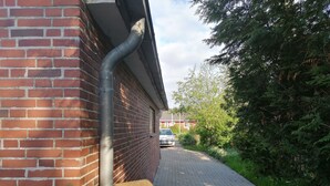 Un bâtiment en briques doté de gouttières et d’un chemin pavé menant à une voiture garée.