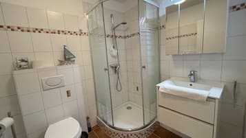 Ein Badezimmer mit Duschkabine, Toilette, Waschbecken und Spiegel.