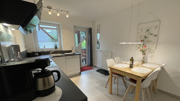 Eine moderne Küche mit schwarzem Arbeitsplatz, weißen Schränken und einem Essbereich mit einem Holztisch und weißen Stühlen.