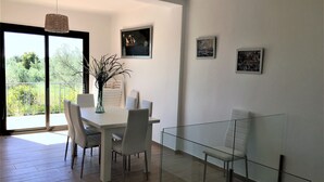 Een moderne eethoek met een witte tafel, vier stoelen, een glazen scheidingswand en een hanglamp.