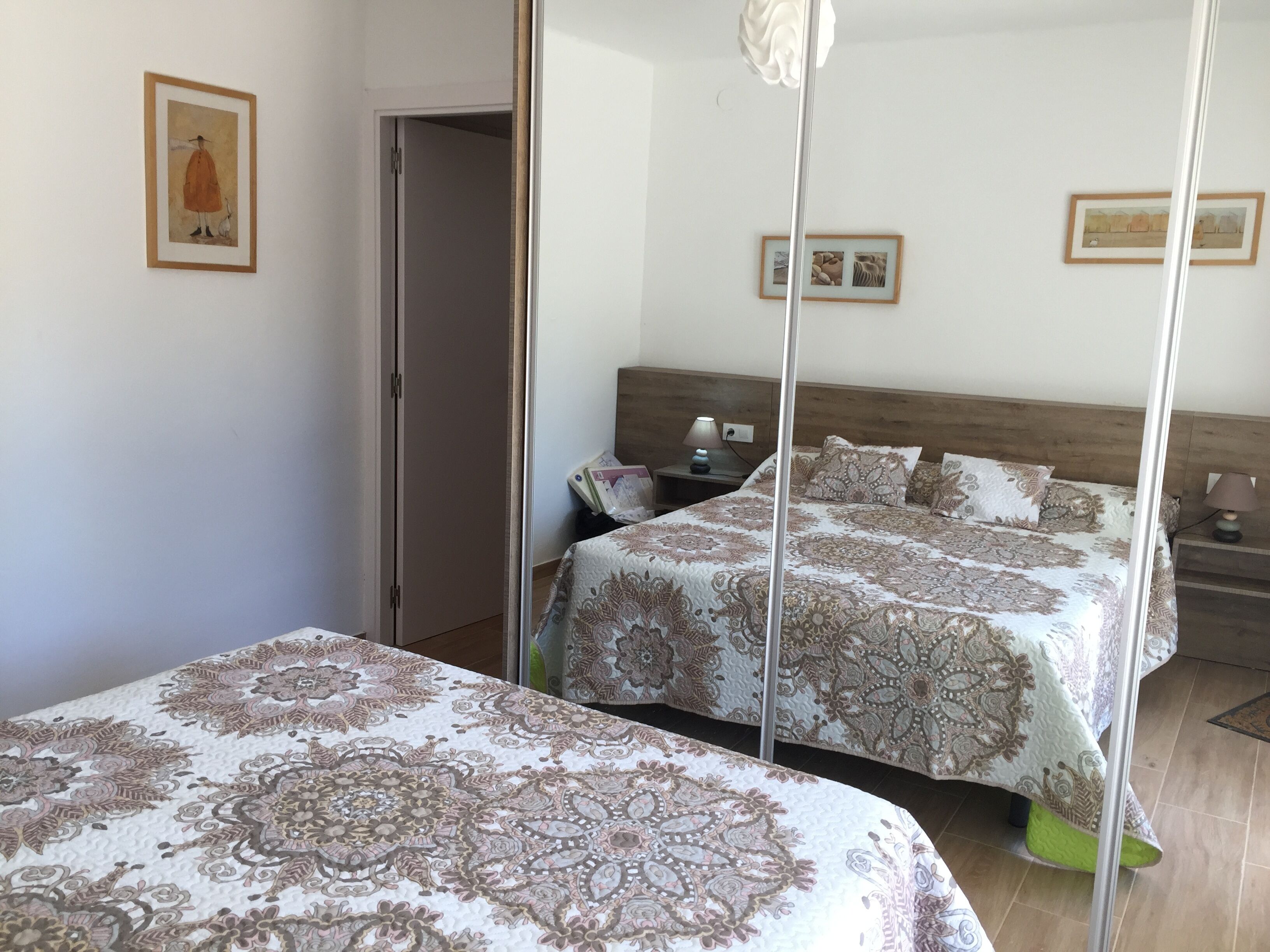 A bedroom with two beds, a wooden headboard, a nightstand with a lamp, and framed artwork on the wall.