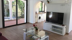 A modern living room with a glass coffee table, a flat-screen TV, and a kitchen area with a washing machine. - Spacious holiday home with private pool, internet, air conditioning (Roses)