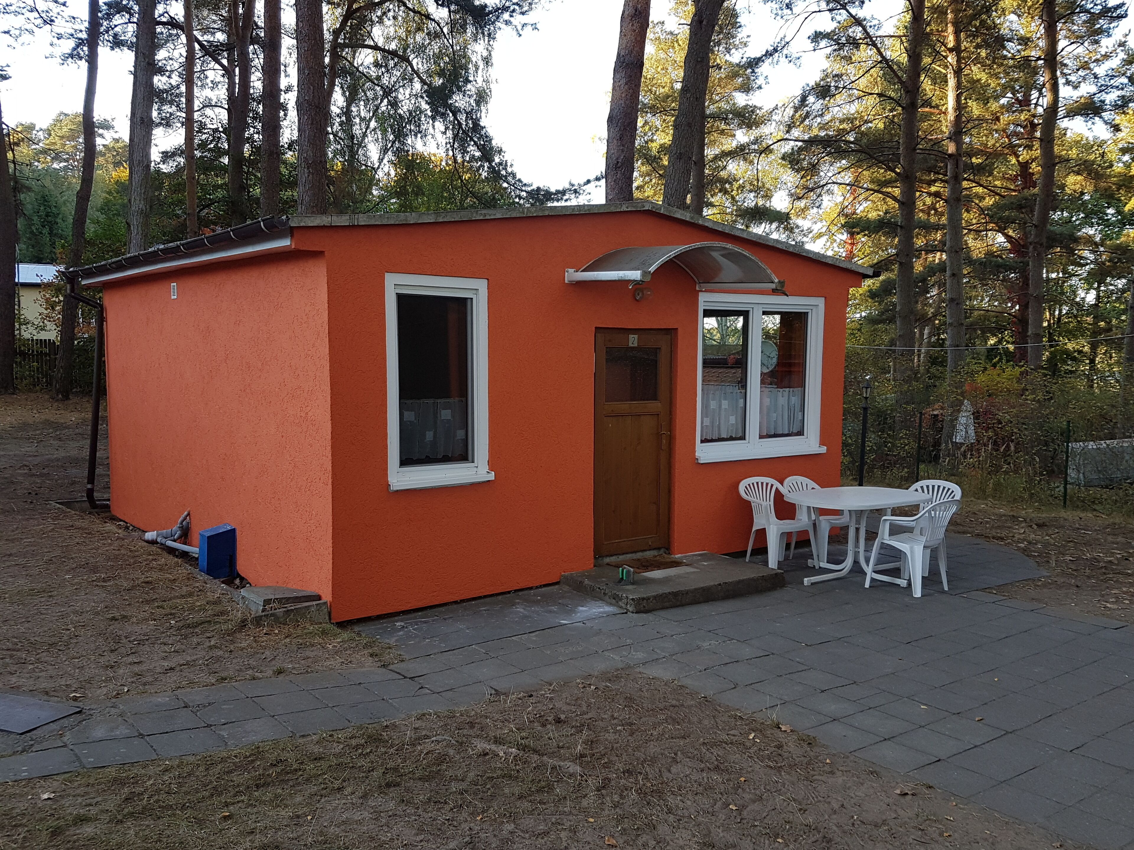 Une petite cabane orange avec une porte, deux fenêtres et une table entourée de chaises à l’extérieur.